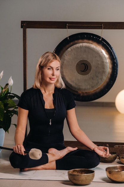 A woman sits with a hammer and next to a gong and Tibetan bowls in the interior