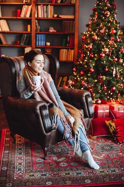 Woman Sitting in an Armchair with Cup in her Hands Interior of House Decorated in New Year39s Decor