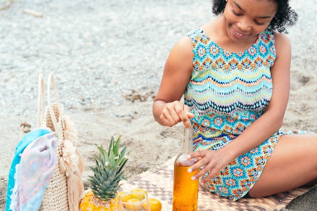 Woman sitting on the beach uncorking a bottle of wine