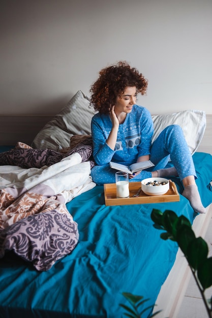 Woman sitting on bed having breakfast with glass of milk and bowl of porridge morning in a cozy warm