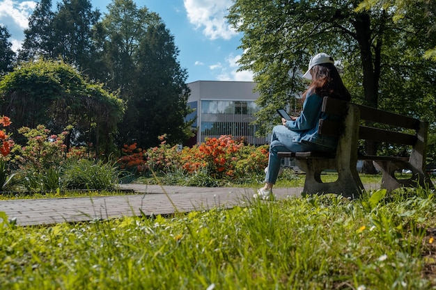 Woman sitting on the bench at city public park reading electronic book