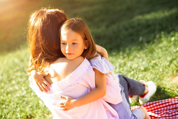 Woman sitting on the blanket in the park while her daughter embracing her