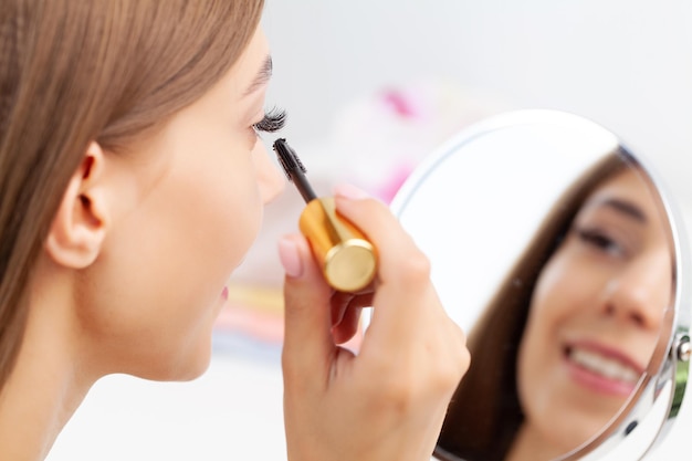 Woman sitting by the mirror and applying makeup