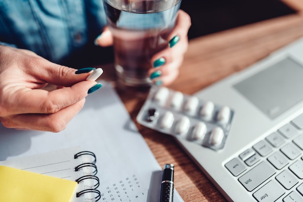 Woman sitting by the office desk and taking medical pills