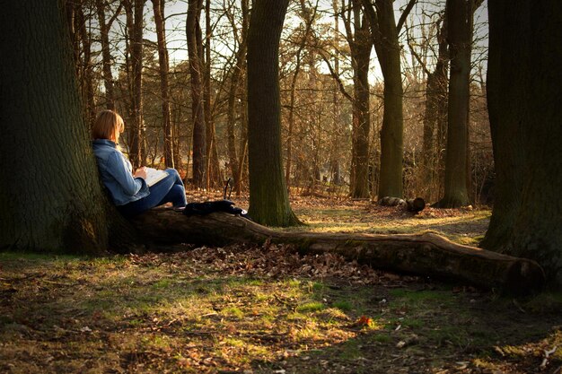 Photo woman sitting by tree trunk in forest