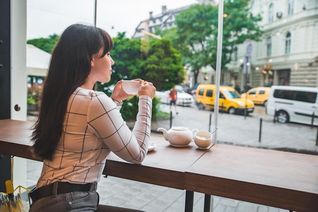 Woman sitting in cafe with big glass window and beautiful view of city street