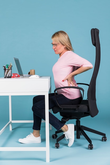 Woman sitting in chair suffering from backache while working on laptop