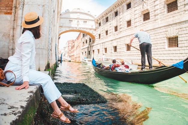 Woman sitting at city quay at venice italy enjoying the view of canals with gondolas copy space