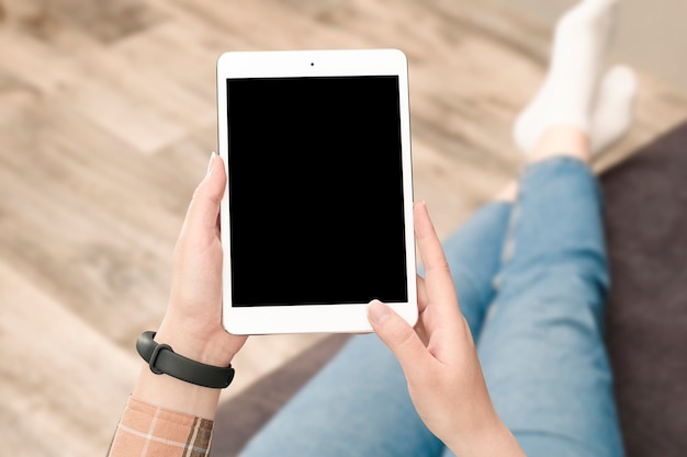 A woman sitting on the couch holds a digital tablet in her hands with a copy space