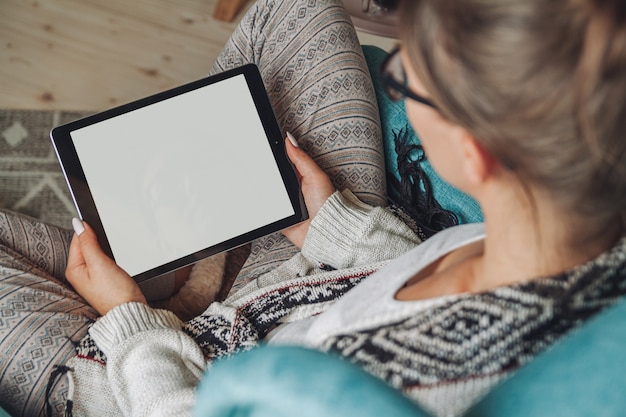 Woman sitting in cozy armchair, with warm blanket, using tablet