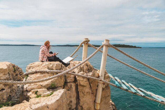 Woman sitting at the edge drawing picture of seascape suspension bridge