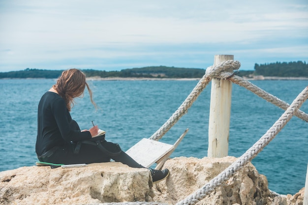 Woman sitting at the edge drawing picture of seascape