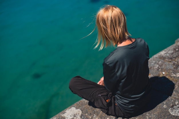 Woman sitting on the edge of the promenade near the ocean