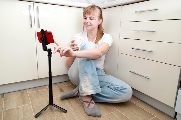 Woman sitting on the floor in the kitchen with a smartphone on a stick