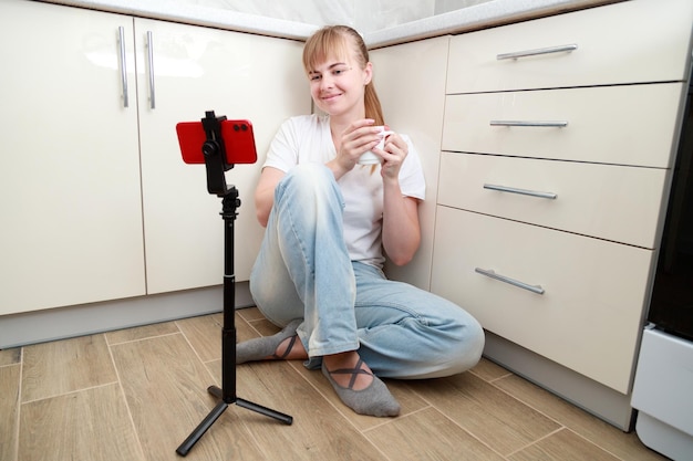 Woman sitting on the floor in the kitchen with a smartphone