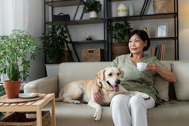 Woman sitting at home on sofa having a cup of coffee next to her dog