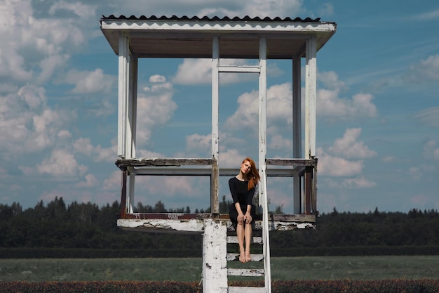 Woman sitting at lookout tower on field against sky