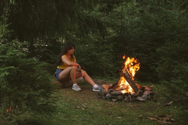 Woman sitting near fire in forest