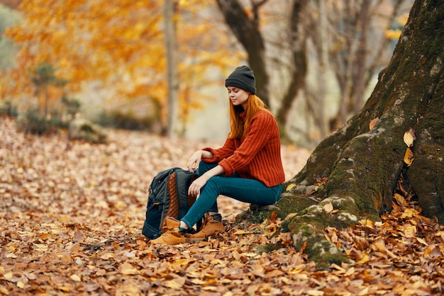 Woman sitting near a tree in autumn forest and falling leaves landscape park High quality photo