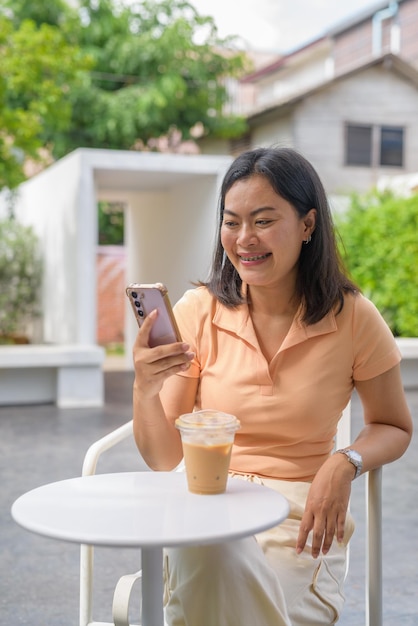 Woman sitting at an outdoor coffee shop casually dressed in an orange top and enjoys an iced coffee