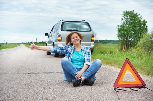 Woman sitting on road near emergency sign showing thumbs up