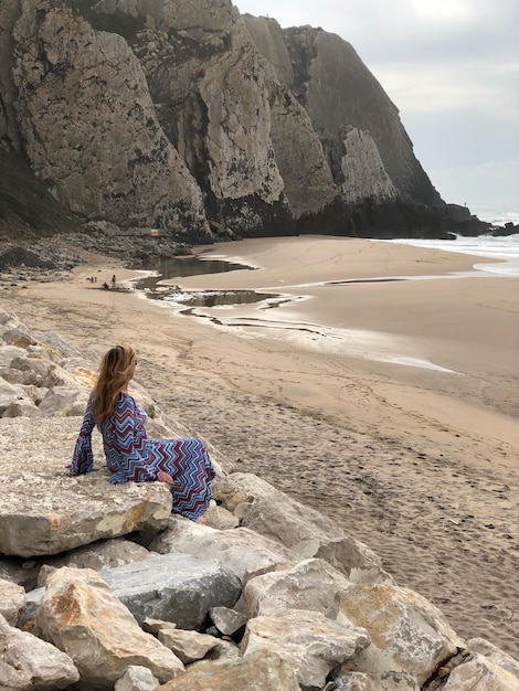 Photo woman sitting on rock by sea against mountain