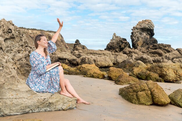 Woman sitting on a rock waving on the beach