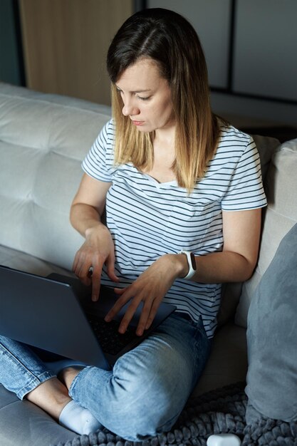 Woman sitting on sofa in living room and using laptop