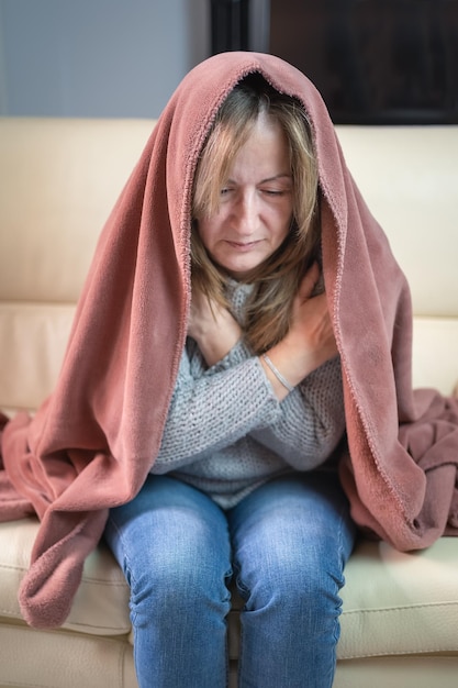 Woman sitting on a sofa and wrapped in a blanket going cold through the winter and energy savings