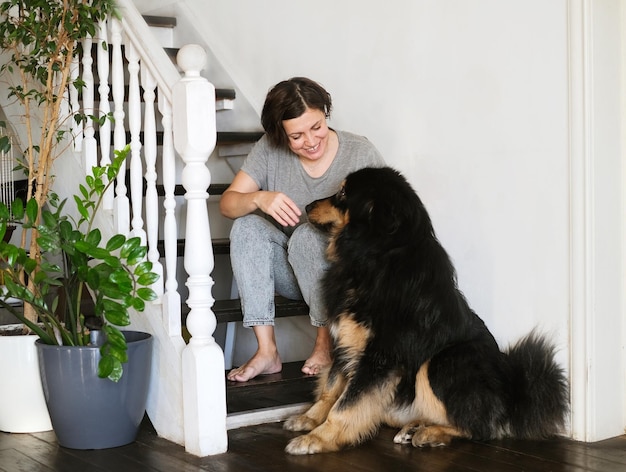 Woman sitting on stairs at home, using smartphone with black big dog