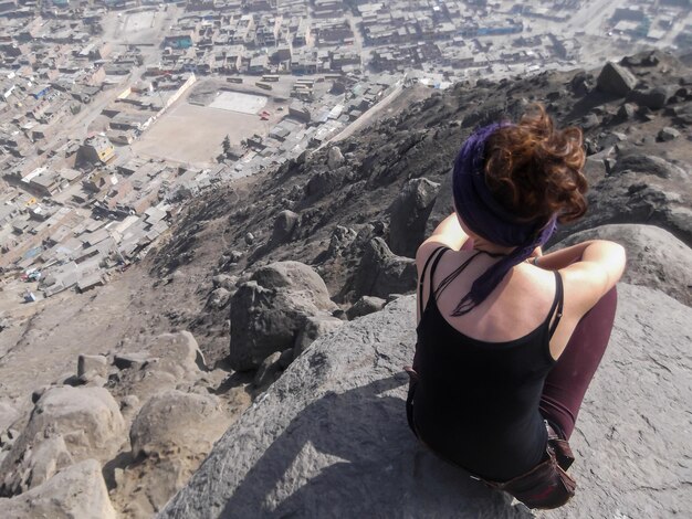 Woman sitting on top of a hill looking at a city in the distance