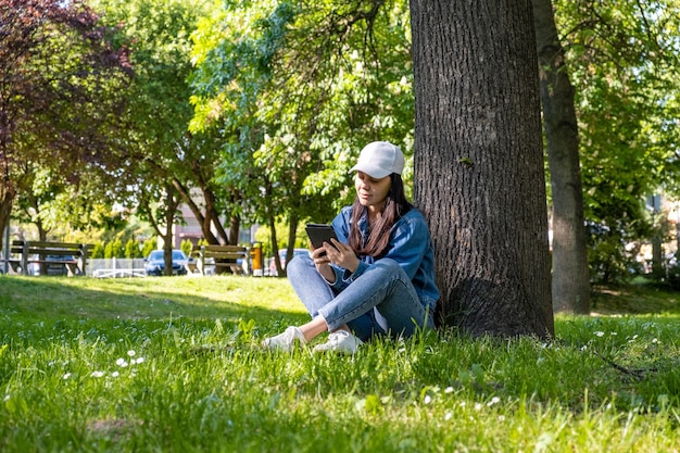 Woman sitting under the tree reading electronic book