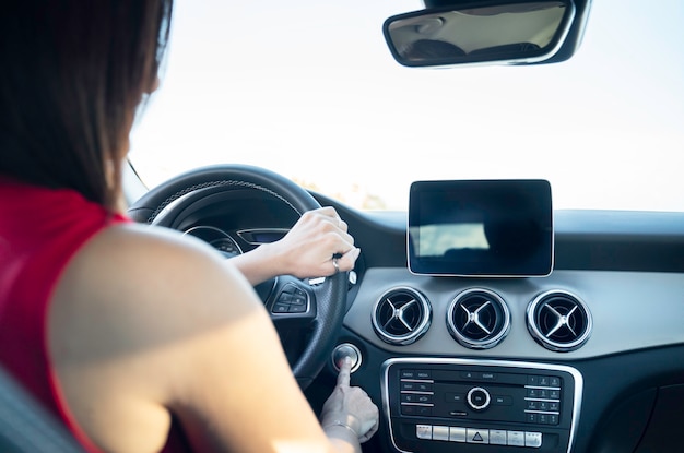 Woman sitting behind the wheel in a car pressing a car ignition button - selective focus.