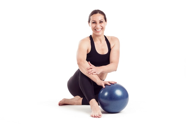 Woman sitting with blue ball in white background smiling