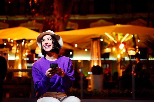 Woman sitting with mobile phone at night on the street