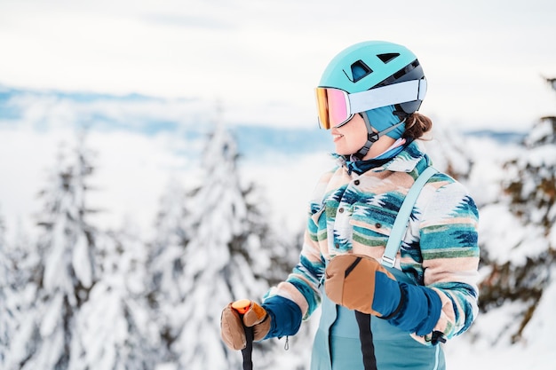 Woman in skiing clothes with helmet and ski googles on her head with ski sticks Winter weather on the slopes On top of a mountain and enjoying view Alpine skier Winter sport