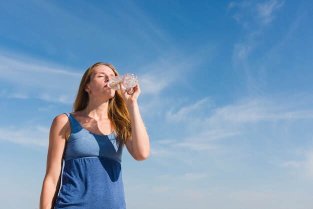 Woman at sky background drink water outdoors