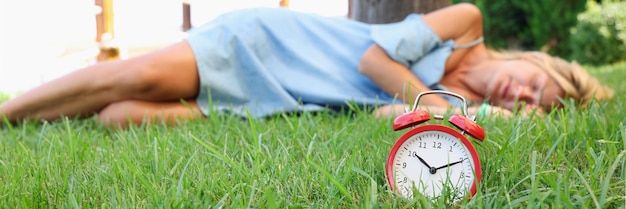 Woman sleeps on grass next to alarm clock dreams and fantasies concept