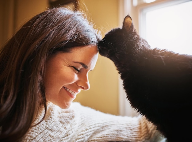 Woman smile and cat kiss in home for love scratch and domestic animal for companion or loyalty Female person pet care and peace in living room or forehead touch for affection sofa and support