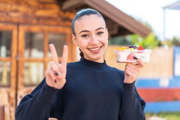 A woman smiles and holds a yogurt with the word breakfast in the background.