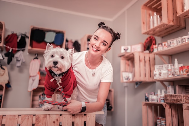 Photo woman smiling. dark-haired appealing young woman smiling after putting red clothing on dog