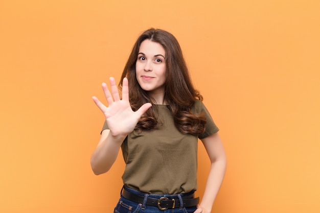 woman smiling and looking friendly, showing number five or fifth with hand forward, counting down