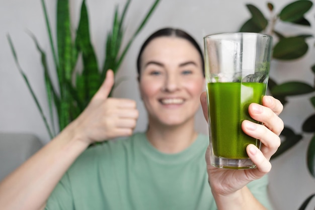 Woman smiling shows a thumbs up She drinking green wheatgrass energy shake