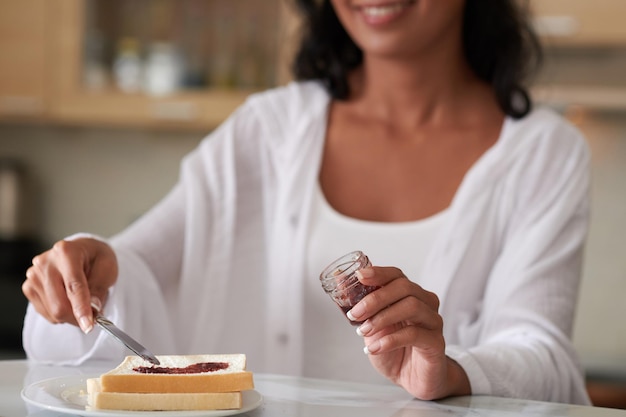 Woman speading homemade jelly from small jar on toast when making breakfast in the morning