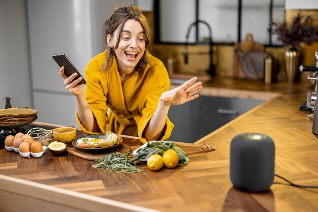 Photo woman speaking to a smart speaker during a breakfast at home