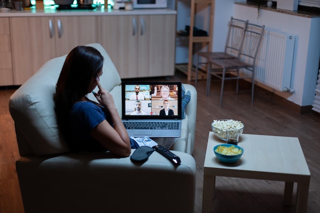 Woman speaking with colleagues on webcam lying on sofa at home