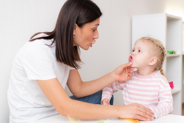 Woman speech therapist helps cute girl to learn correct pronunciation and competent speech in her office