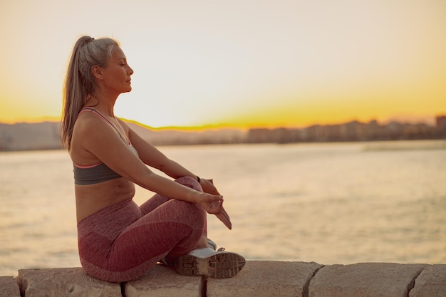 Woman in sportewear meditating in lotus position at seaside