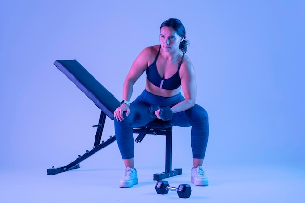 Woman in sportswear doing biceps exercises sitting on a bench