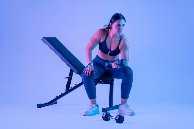 Woman in sportswear doing biceps exercises sitting on a bench